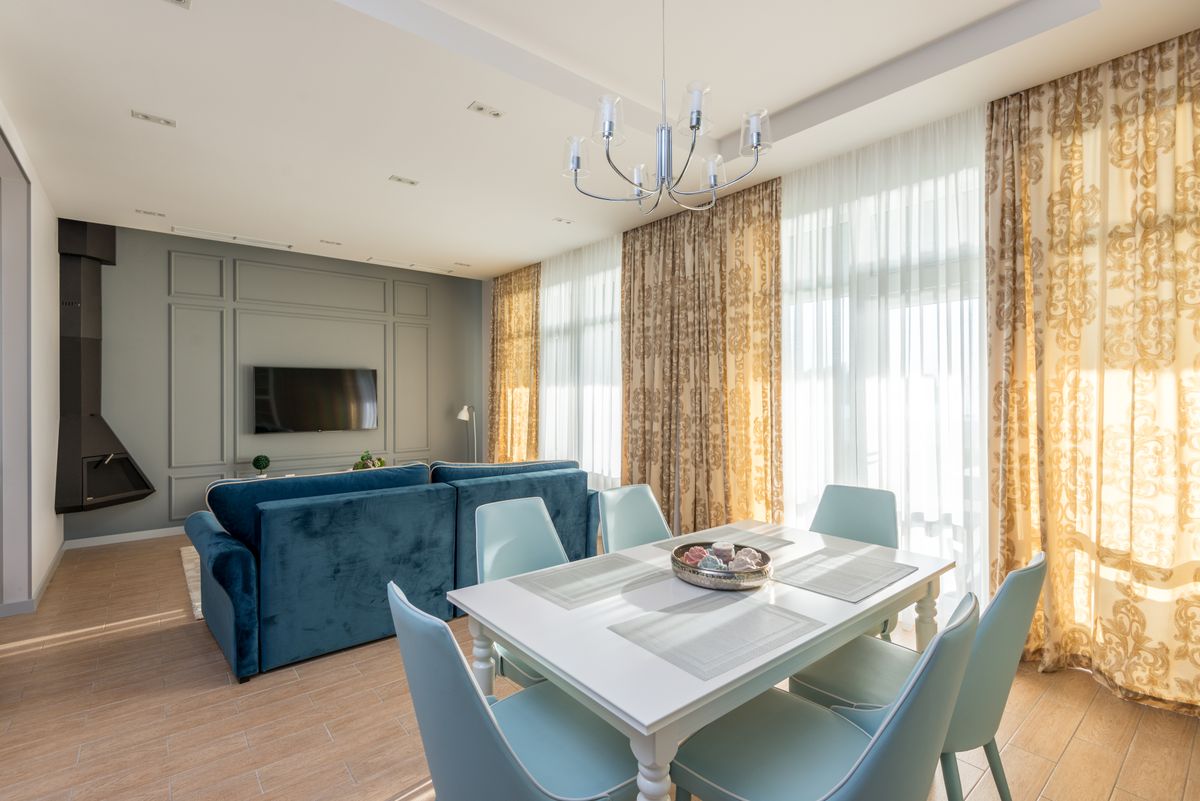Lichte woonkamer met houten vloer, hoge ramen en een blauwe bank